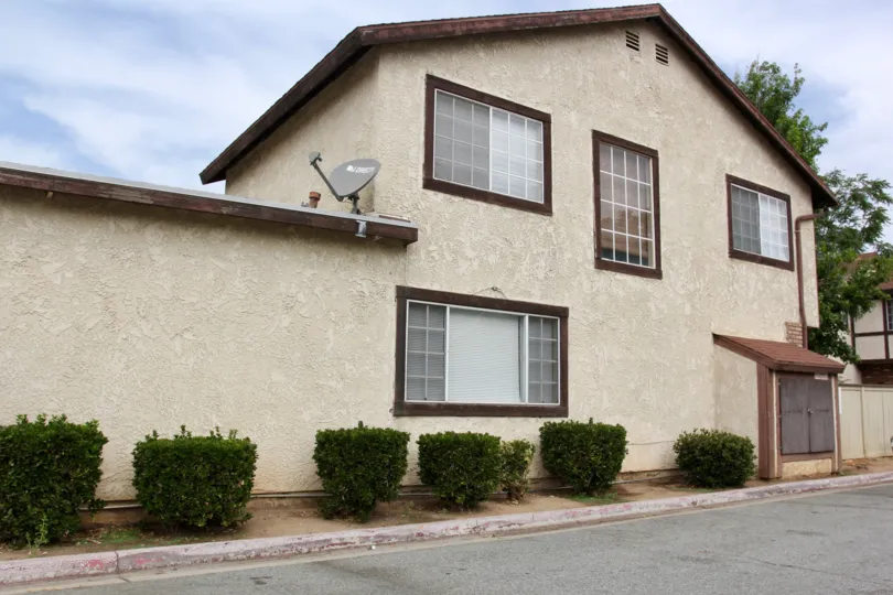 Side view house of shrubs and large windows with satellite dishes