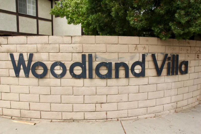 A cream colored brick welcome structure with black letters displaying Woodland Villa, in Moreno Valley, California