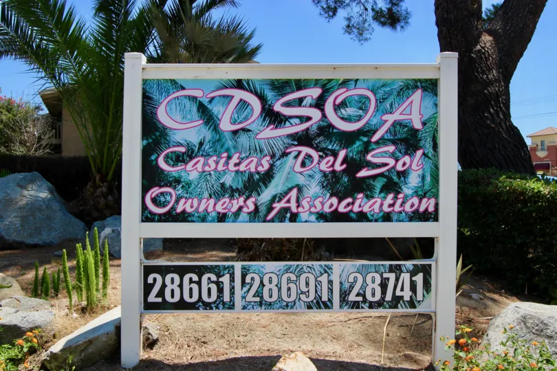 A mural of palm tree sits behind lettering on a sign in Casitas Del Sol community.