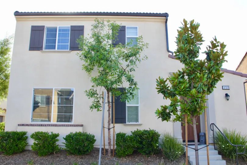 boxy house with spanish roof and shutters on windows with brand new trees and shrubs