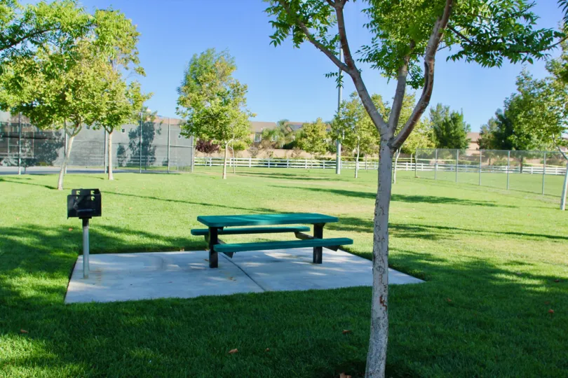 A small bench and a barbecue at a fenced in park of the Paseos at Crown Valley