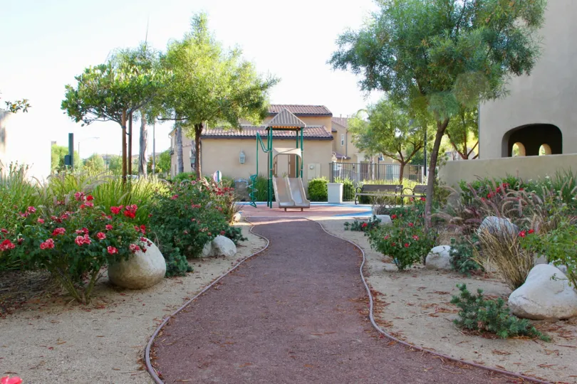 The pathway full of flowers and green foliage leading to a child's playground with slide.