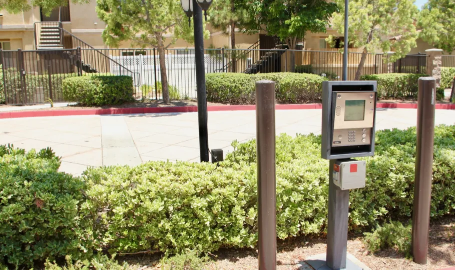 Gated entrance call box with shrubs, lamp posts and manicured trees
