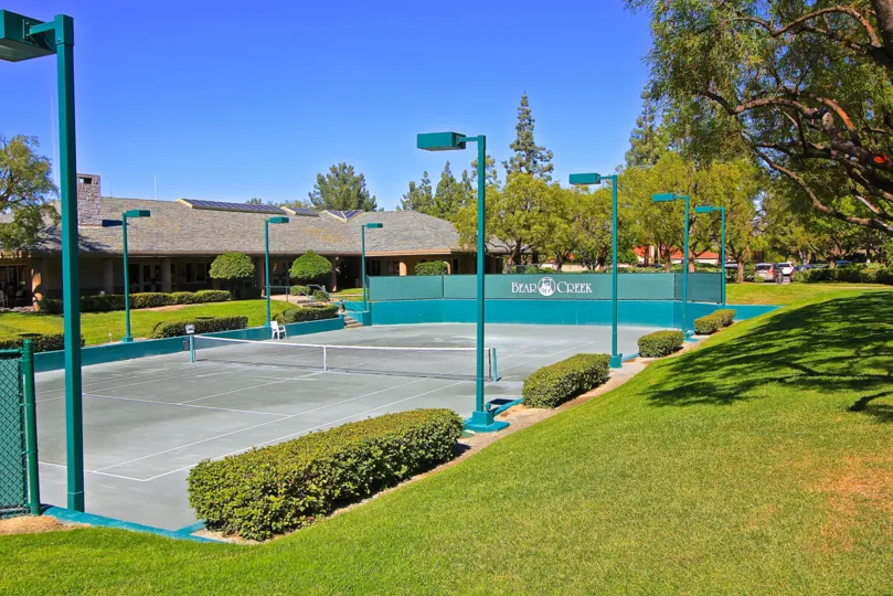 Tennis courts of the Retreat at Bear Creek community with lights and bushes.