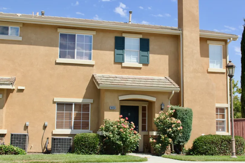 Pink condo with air conditioners and pleasant shrubs line the entrance to this condo