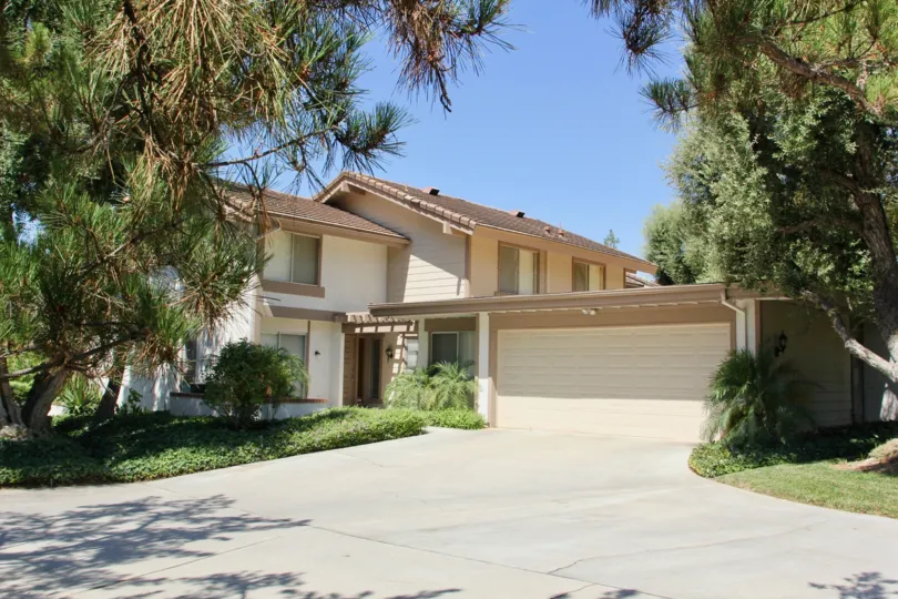 House nested in large trees with garage and manicured lawn and gardens