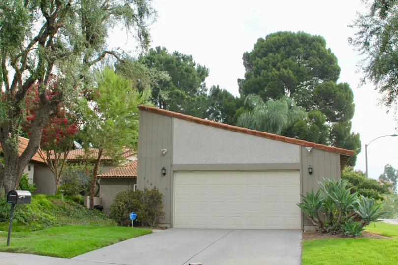 post box is placed in front of house andfull of tree and grasses are surrounded the house