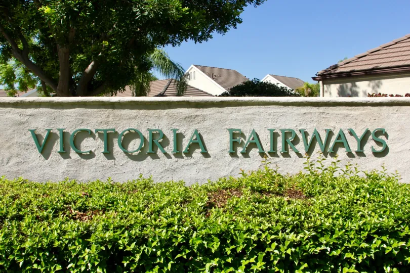 Entrance sign of VIctoria Fairways is among trimmed hedges and large shade trees