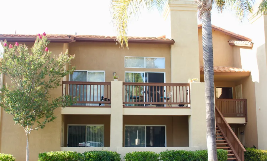Double story condo with balconies and trees with shrubs and palm trees