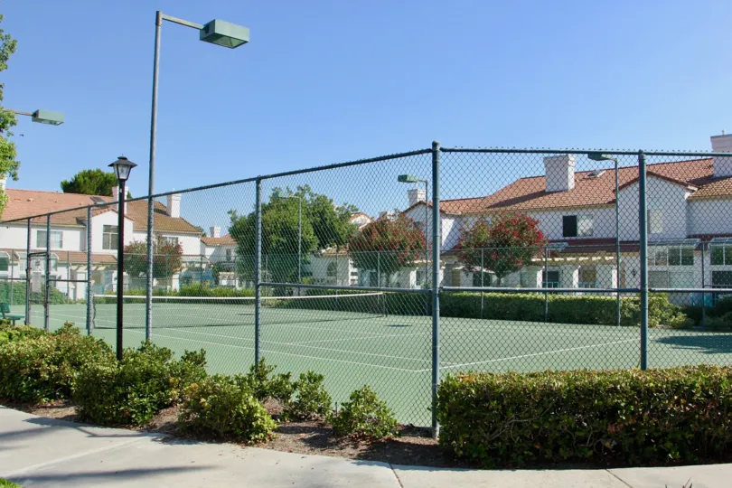 Fenced in tennis court surrounded by white townhomes in Rancho Del Mar