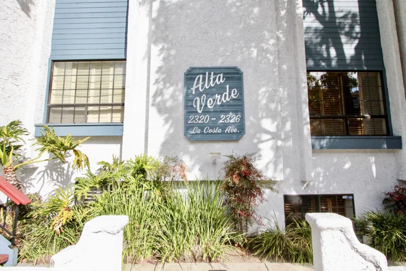 Building with a sign and bushes and windows in the Alta Verde Community in Carlsbad, CA.