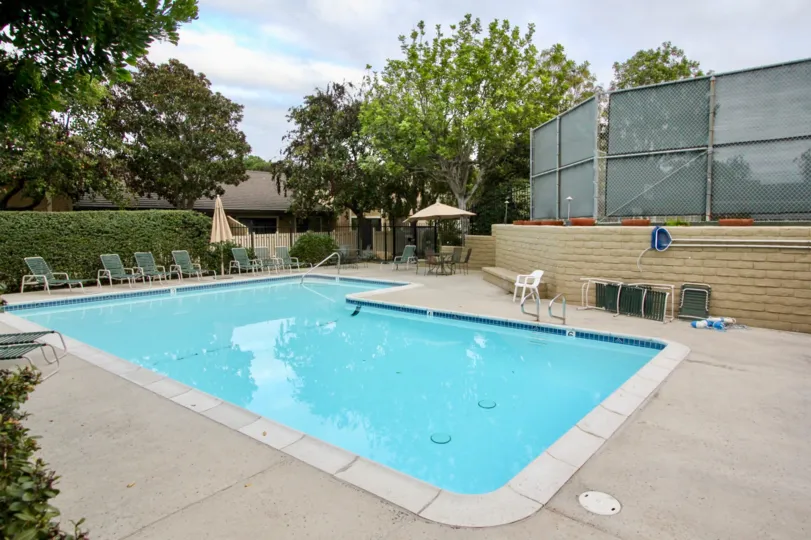 THE BUILDING IN THE CARLSBAD PALISADES WITH THE SWIMMING POOL, CHAIRS, PLANTS, TREES