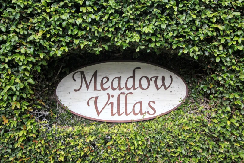 An oval sign with the words "Meadow Villas" surrounded by plants