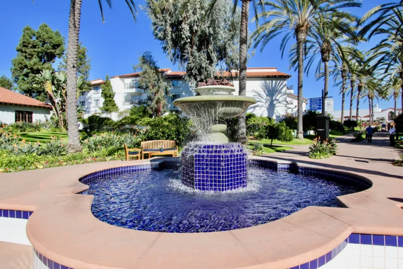 A beautiful water fountain in the Omni La Costa Resort & Spa with some lawn, shrubs and trees also.