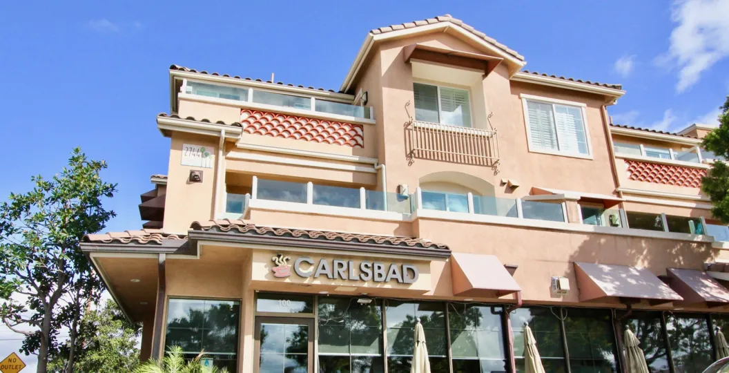 A pink building with many windows sits below a blue sky in Village by the Sea in Carlsbad CA