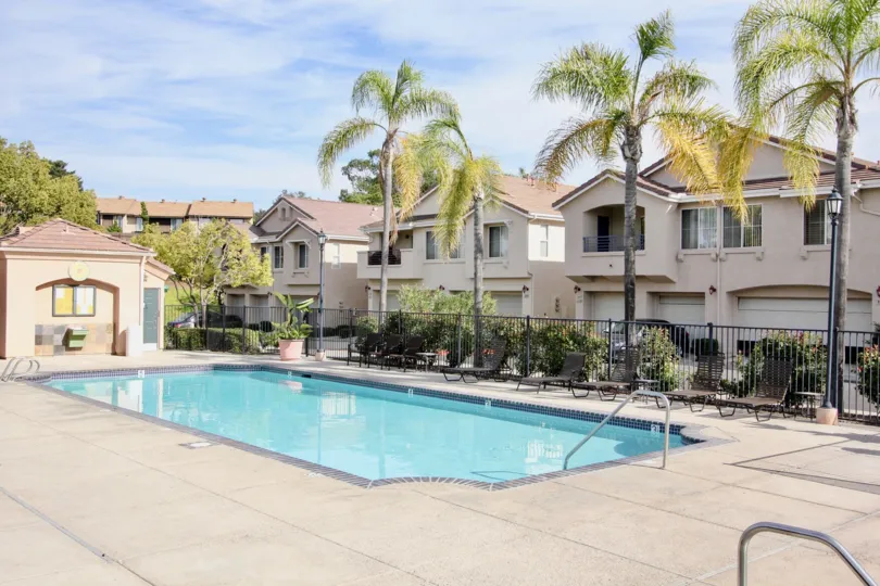 Pool area with patio and lounge area with four palms next to condos in Chula Vista, CA.