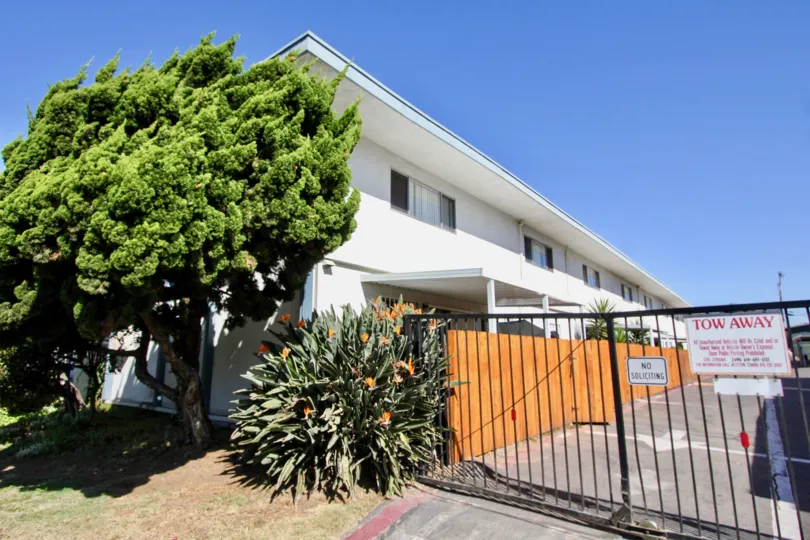 Front gate view of the building with trees plants and flower in front of the Gate and TOW AWAY board in front of gate in Chula Vista Townhomes