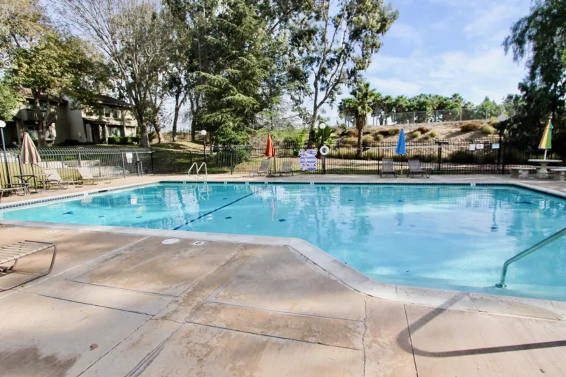 Asymmetrical swimming pool at Encore Bonita community in Chula Vista, CA. Partially shaded patio with lounge chairs and closed umbrellas.