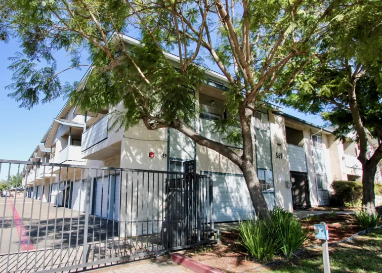 2 story eggshell apartment complex with 1 car garage and balcony with trees.