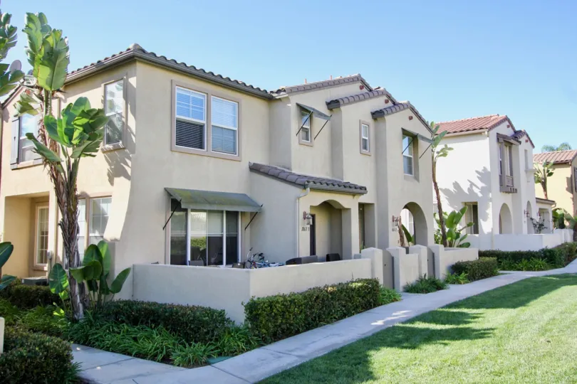 A nice housing community with similar looking houses, green grass, tall trees, patios, and nice walk ways