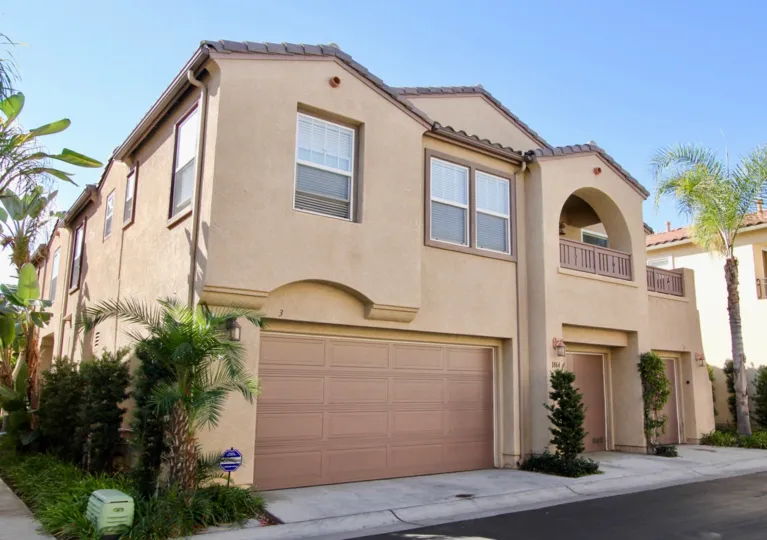front view of a beautiful dark gold building with multiple car garages, plants, and an upstairs patio