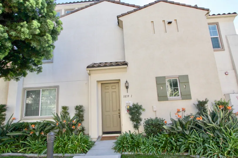 A tall white door in the front of a white town home surrounded by flowers in Hearthstone Village in Chula Vista CA