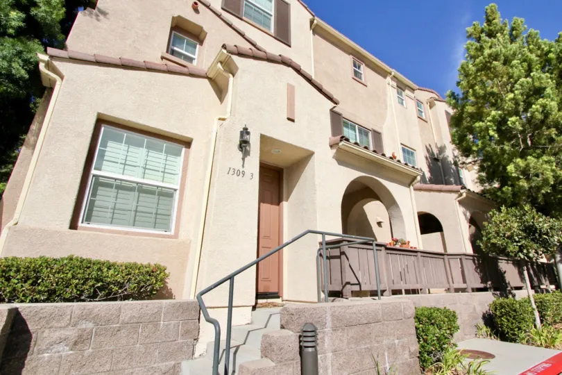 Two story pink building with pink doors with tall trees in front at Hearthstone Village in Chula Vista CA