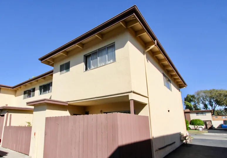 A two story brown building with a wooden pink fence at Holiday Gardens in Chula Vista California