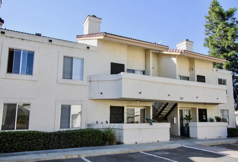 2 story white apartment complex with shared balcony on a sunny day.