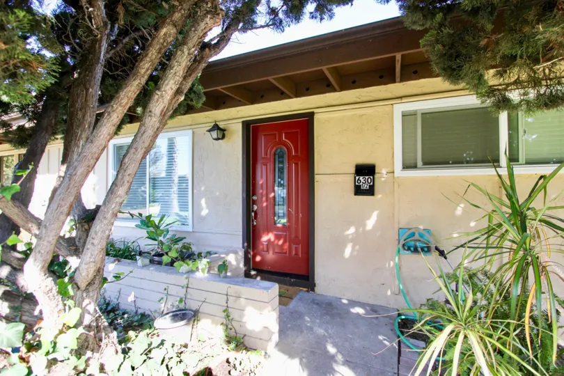 A large tree stands in front of a red door of a home at the Karen Condominiums in Chula Vista, CA.