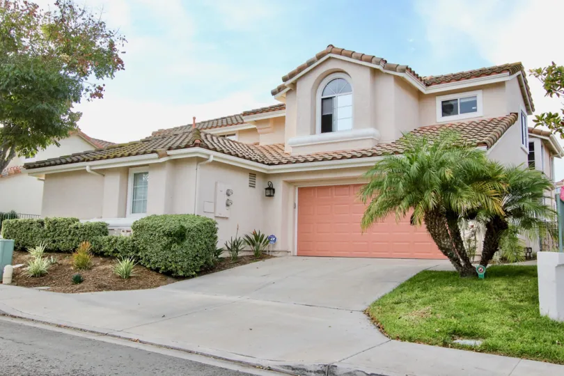 Two-car garage with coral pink door and driveway of Mediterranean home.