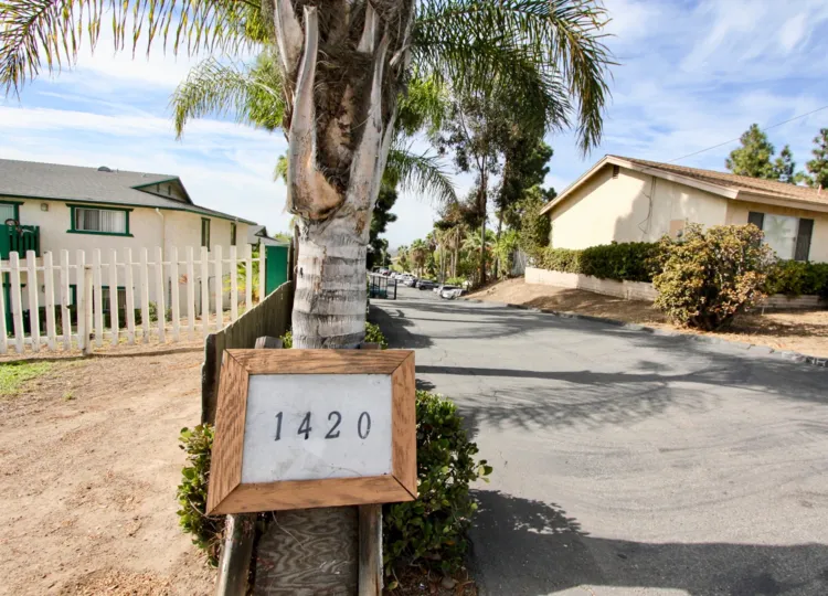 a sign that says 1420 which is on a tree with houses behind