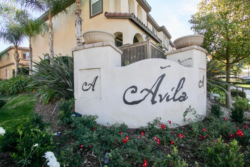 Front sign of Villas De Avila with beautiful landscaping of trees and flowers in Chula Vista, Ca.