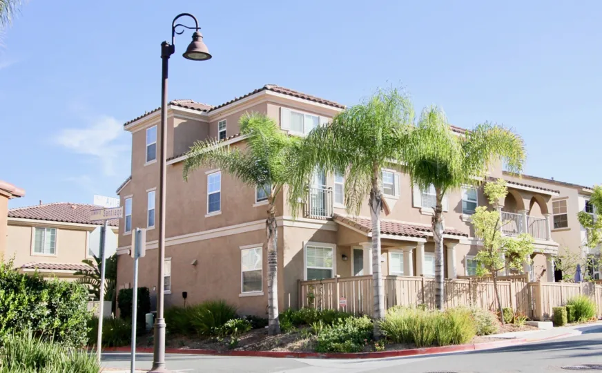 Front of apartments at Villas De Avila with palm trees and wooden fence in the front in Chula Vista, Ca.