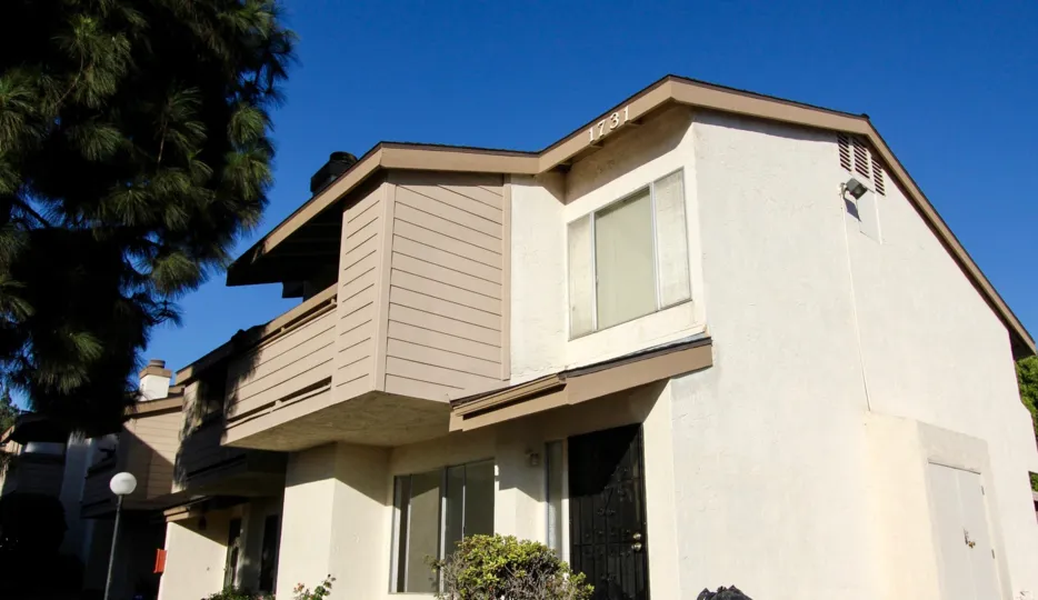 A sunny day in the area of Woodside Village, outside, trees, blue sky, sliding glass doors, bushes, balcony