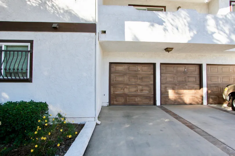 A tan vehicle sits in front of three garage doors on a white residential building in the Blossom Park community in College Area California