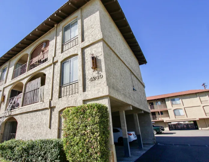 A tall hedge sits against a beige stucco building at Menlo Ave condos