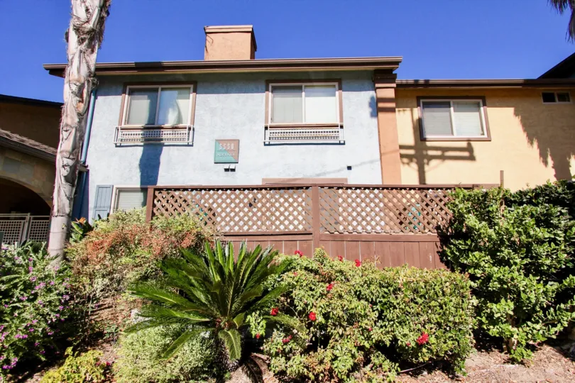Two story housing buildings next to a fence and green plants at The Court at Adelaide in College Area California