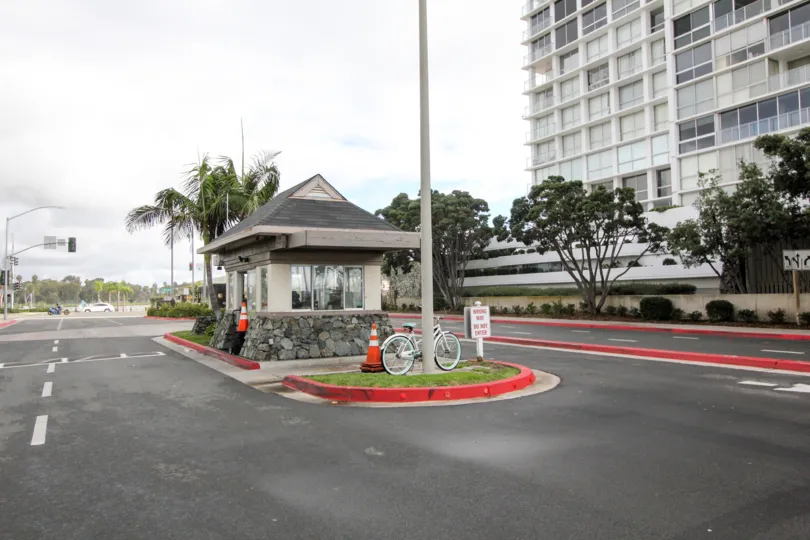 The entrance to a parking lot with a guard cabin, some cones and a bike, and a big building in the back in Coronado Shores, Coronado, CA