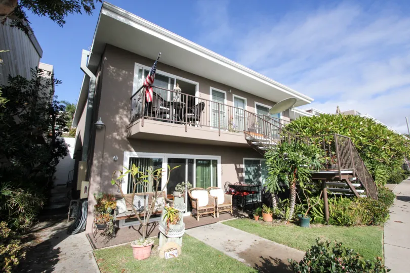 A gray house with a balcony and a lawn in front with bushes during a sunny day in Glorietta Bay, Coronado, CA