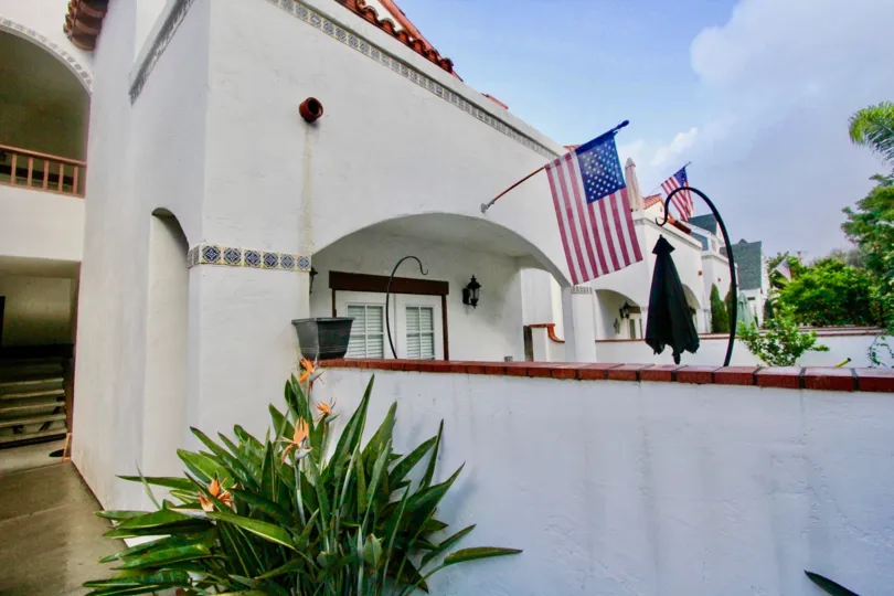 A white house with an American flag and some bushes in front during a sunny day in Rancho Las Palmas, Coronado, CA