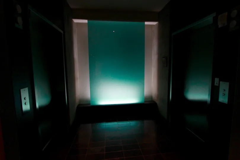 A single light pointed upwards illuminates a teal wall.