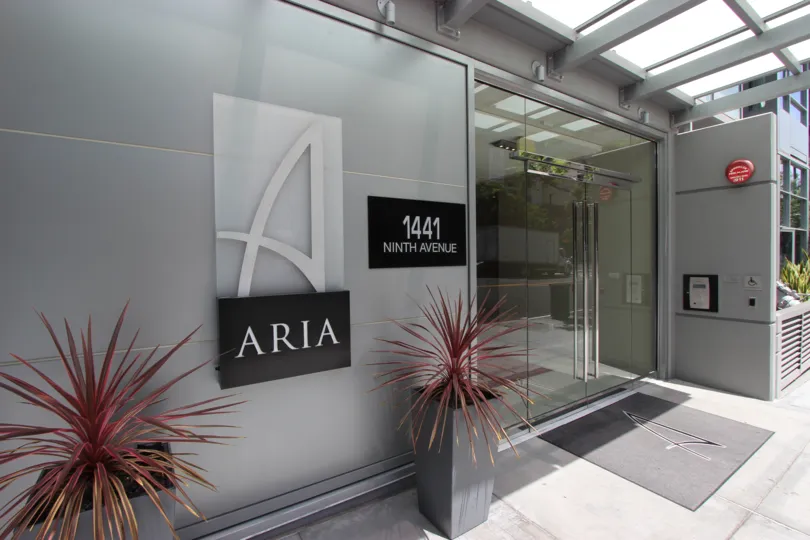 The entry doors to Aria with welcoming plants and signage.