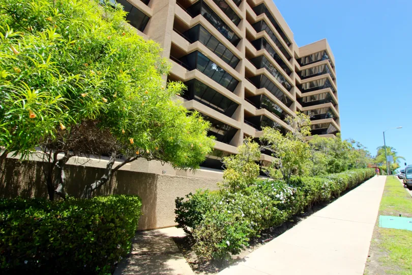 Sidewalk lined with plants and trees beneath condominiums at Brittany Tower in Downtown San Diego CA
