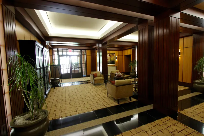 Dark wood colomns frame the seating area inside the Cityfront Terrace with beige carpet, black tiles, and recessed lighting in the ceiling.