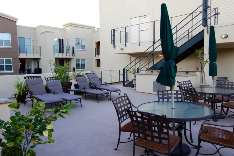 A view of the outdoor terrace dining area, staircase, and balconies at the Crown Bay apartment complex on a sunny afternoon.