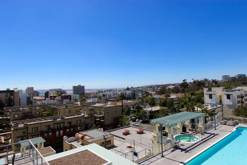 Downtown San Diego building in the Discovery community in California. The view from the roof of a building of a large part of the city and blue sky in the background. Pool and hot tub are pictured on the bottom right.