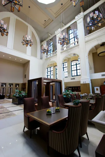 A view of the lobby of the Electra building with modern light fixtures, cathedral ceiling, and skylights over comfortable dining tables.