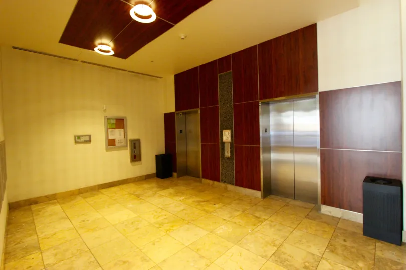 Two silver elevators sit on a wall with wood paneling in Downtown San Diego, CA