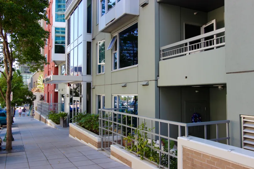 Sidewalk lined with a tall gray building and trees at La Vita in Downtown San Diego CA